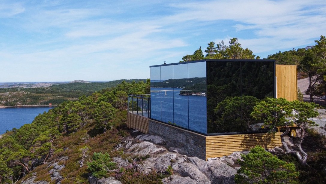 Mirrored cabin on a rocky cliff above a fjord