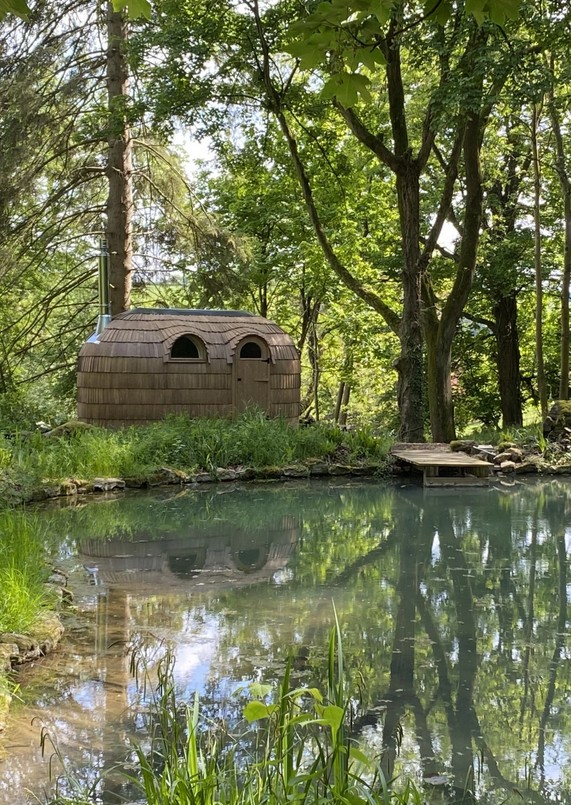 Wooden iglu reflected in a quiet woodland pond